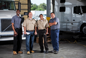 Image of four smiling long haul truckers and their trucks