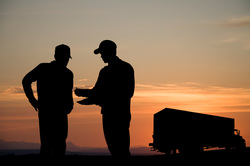 Image of truck driver, customer, and truck against the sunset